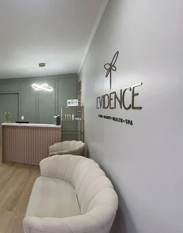 Nome Evidence em relevo na parede da recepção, sobre a bancada e as poltronas claras da clínica.